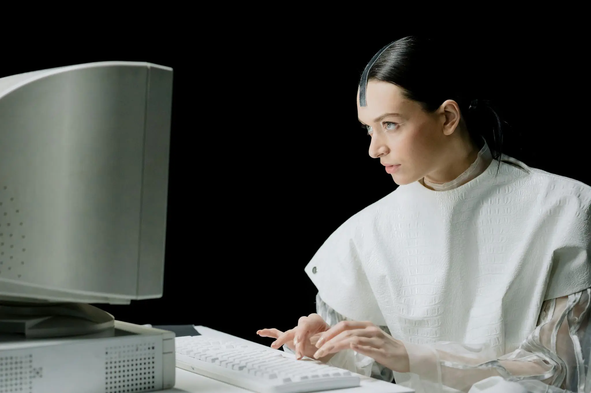 A woman in futuristic attire types on a vintage computer, blending old and new technology.